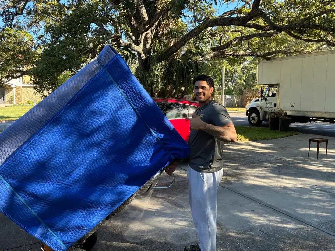 Panther Moving crew member carrying furniture wrapped in a protective blanket